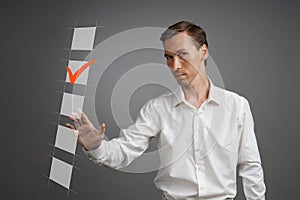 Young business man in white shirt checking on checklist box. Gray background.