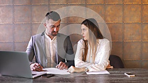 Young business man and woman sitting in cafe and discussing contract