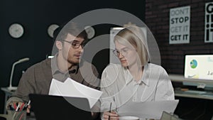 Young business man and woman working together front laptop in dark office