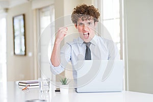 Young business man working with computer laptop at the office angry and mad raising fist frustrated and furious while shouting