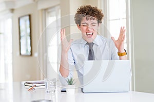 Young business man working with computer laptop at the office celebrating mad and crazy for success with arms raised and closed