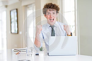 Young business man working with computer laptop at the office celebrating surprised and amazed for success with arms raised and