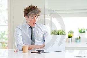 Young business man working with computer laptop at the office scared in shock with a surprise face, afraid and excited with fear