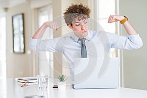 Young business man working with computer laptop at the office showing arms muscles smiling proud