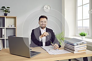 Young business man working at the desk on his workplace at office, looking at the camera smiling.