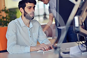 Young business man working on desktop computer at his desk in modern bright startup office interior