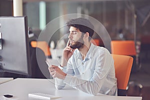 Young business man working on desktop computer at his desk in modern bright startup office interior