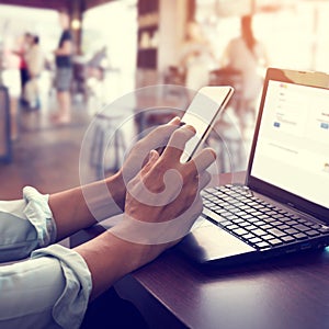 young business man working on his laptop and using smart phone sitting at wooden table in a coffee shop