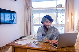 Young business man working at home in his bedroom with laptop and papers on desk. Home office concept