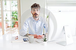 Young business man working using computer afraid and shocked with surprise expression, fear and excited face