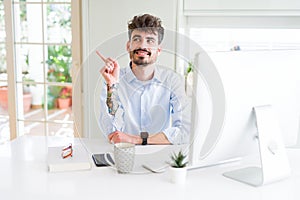 Young business man working using computer with a big smile on face, pointing with hand and finger to the side looking at the