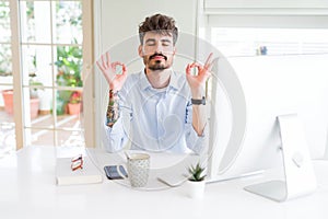 Young business man working using computer relax and smiling with eyes closed doing meditation gesture with fingers