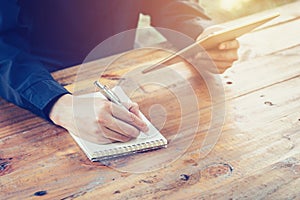 Young business man writing note pad and using tablet in coffee s