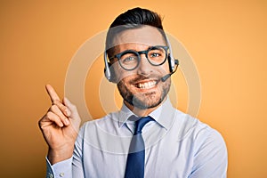 Young business operator man wearing customer service headset from call center with a big smile on face, pointing with hand and