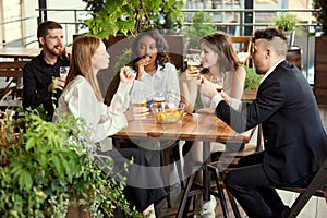 Young business people, colleagues meeting together at cafe, bar after work to drink beer, talk and spend relaxing time