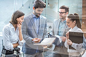 Young business people discussing over business report while standing in office hallway