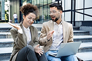 Young business people fellow teamworkers sit on the stairs of the office building argue and cannot find a common solution to the