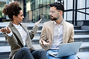 Young business people fellow teamworkers sit on the stairs of the office building argue and cannot find a common solution to the