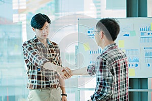 Young business people shaking hands Two handsome young men shake hands with smiles at the office with a colleague with a graph in