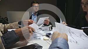 Young business people sitting at table and discussing income charts and graphs at the end of working day. Business team