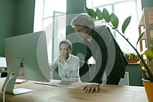 Young business people working with computer. Caucasian man wearing formalwear and his female colleague look at monitor