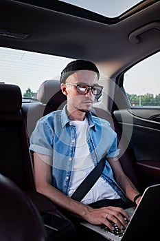Young business person using laptop on a backseat of a car.