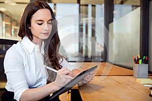 Young business professional at office workspace sitting at desk writing on tablet with electronic stylus pen, writer, journalist,