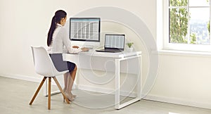 Young business woman accountant working on a laptop with tables at modern white office.