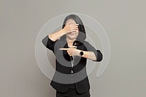 Young business woman in black suit is pointing to the left while covering her eyes with her hands