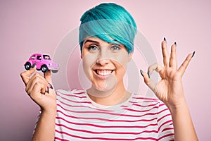 Young business woman with blue fashion hair holding small car as rental and insurance doing ok sign with fingers, excellent symbol