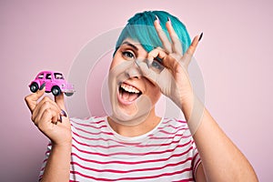 Young business woman with blue fashion hair holding small car as rental and insurance with happy face smiling doing ok sign with