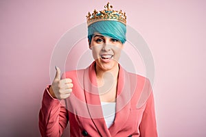 Young business woman with blue fashion hair wearing queen crown over pink isolated background doing happy thumbs up gesture with