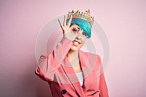 Young business woman with blue fashion hair wearing queen crown over pink isolated background doing ok gesture with hand smiling,