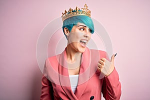 Young business woman with blue fashion hair wearing queen crown over pink isolated background smiling with happy face looking and