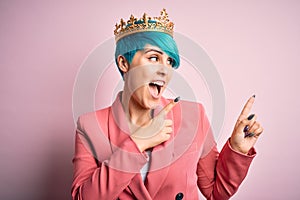 Young business woman with blue fashion hair wearing queen crown over pink isolated background smiling and looking at the camera