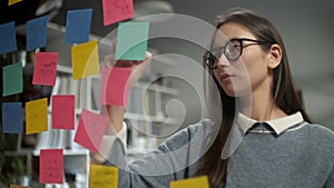 Young business woman brainstorming. Asian woman writing down ideas on sticky notes attached to glass wall. Business