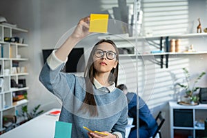 Young Business Woman Brainstorming. Asian Woman Writing Down Ideas On Sticky Notes Attached To Glass Wall. Business