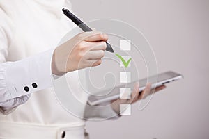 Young business woman checking on checklist box. Gray background.