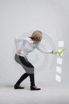 Young business woman checking on checklist box. Gray background.