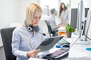 Young business woman with clipboard working in front of computer at her workplace.