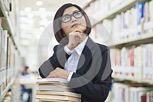 Young Business Woman Contemplating and Looking Up in Bookstore with a Stack of Books