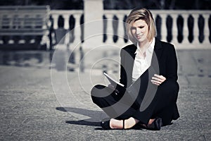 Young business woman with a folder sitting on city sidewalk