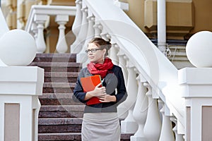 Young business woman hold in hand folder against office building on street near stairway