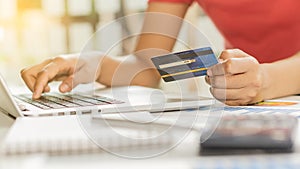 A young business woman holding a blue credit card in hand and using a laptop computer to shop online and dial the number on the