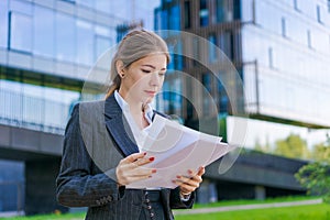 Young business woman holding papers in business clothes on city street against