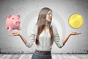 Young business woman holding pink piggy bank and golden dollar coin in her hands on grey wall background