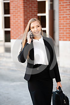 Young business woman leaving her job with hand bag in her hand talking on smart phone