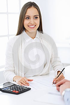 Young business woman and man sitting and working with computer and calculator in office. Bookkeeper checking balance or