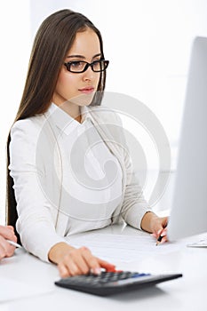 Young business woman and man sitting and working with computer and calculator in office. Bookkeeper checking balance or