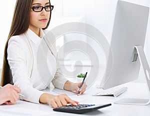 Young business woman and man sitting and working with computer and calculator in office. Bookkeeper checking balance or